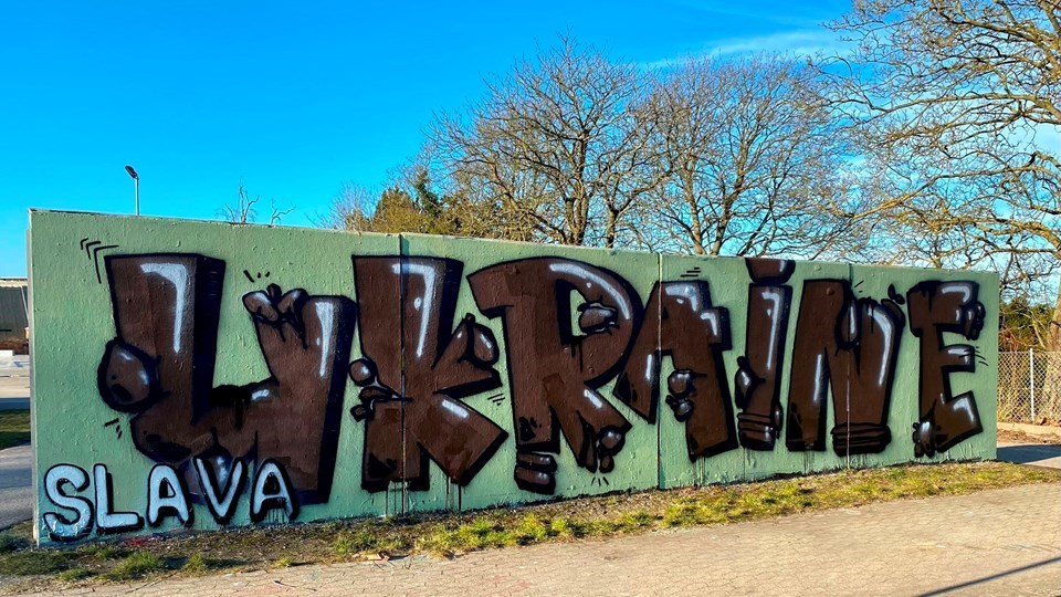 Grafitti-værk med teksten "Slava Ukraine" og blå himmel med hvidlige skyer